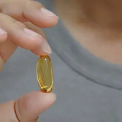 Dłoń trzyma żółtą kapsułkę. Czy suplementy omega-3 6 9 mają skutki uboczne?