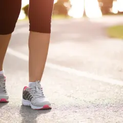 Kobieta w sportowych butach biegnie po asfaltowej ścieżce. Czy bieganie odchudza? Tak, regularny wysiłek pomaga spalić kalorie i osiągnąć wymarzoną sylwetkę.