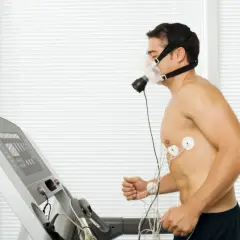 Mężczyzna w masce tlenowej i elektrodach biegnie na bieżni podczas testu wysiłkowego.