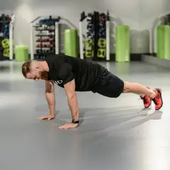 Mężczyzna wykonuje pompki, angażując mięśnie klatki piersiowej, ramion i brzucha.