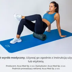 Kobieta na macie rehabilitacyjnej roluje mięsień piramidowy za pomocą wałka.