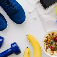Niebieskie buty sportowe, hantle, miska owsianki z owocami, jabłko, telefon i butelka wody.