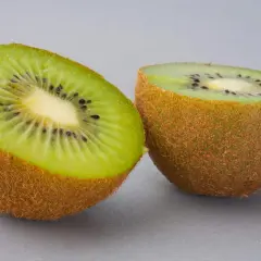 Dwa połówki kiwi na szarym tle. Zastanawiasz się, ile kalorii ma kiwi? To niskokaloryczny owoc, idealny na zdrową przekąskę.