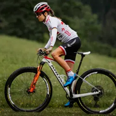 Kobieta w stroju kolarskim jedzie na rowerze górskim, utrzymując optymalną kadencję na trawiastym podłożu.