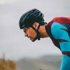 Kolarz w kasku i sportowym stroju pochylony nad kierownicą.