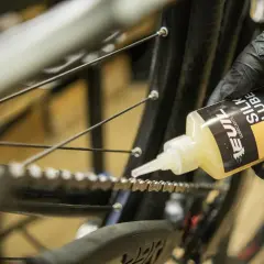 Rękawiczka z czarną rękawiczką aplikuje olej do łańcucha rowerowego. Płynny smar do łańcucha zapewnia płynną jazdę.