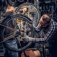 Dwóch mechaników pracuje nad rowerem w warsztacie. Jeden z nich dokonuje konserwacji roweru, dokręcając śruby kluczem.