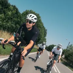 Trzech kolarzy w kaskach i okularach ściga się po asfaltowej drodze, osiągając tętno maksymalne.