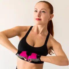 Kobieta w sportowym topie wykonuje ćwiczenia na podniesienie biustu, z różowymi rękawiczkami na dłoniach.