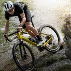Kolarz na żółtym rowerze gravel pokonuje kamienisty szlak. To właśnie gravel, czyli rower do jazdy po różnym terenie.