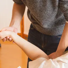 Fizjoterapeuta pomaga pacjentowi w ćwiczeniach po zabiegu cieśni nadgarstka, delikatnie masując przedramię.