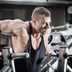 Mięśniowy mężczyzna wykonuje pompki na poręczach, jedno z najlepszych ćwiczeń na triceps.