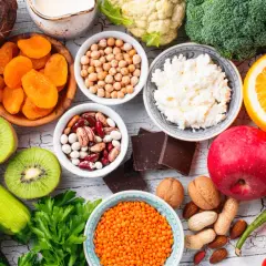 Kolorowy stół pełen zdrowych produktów: cukinia, kiwi, pomidory, bakłażan, jabłko, pomarańcza, brokuły, kalafior, soczewica, ciecierzyca, fasola, orzechy, migdały, suszone morele, ryż, twaróg i gorzka czekolada – idealne warzywa o niskim indeksie glike...