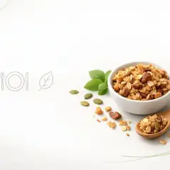 Chrupiąca granola w miseczce i na łyżce, obok pestki dyni i listki bazylii. To idealny pomysł na zdrowe śniadanie.