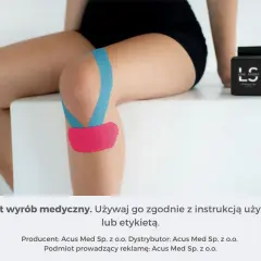 Kolano z niebieskim i różowym plastrem, wspierające mięsień po zerwaniu. Obok pudełko plastrów.