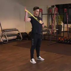 Mężczyzna wykonuje ćwiczenie rotacja zewnętrzna ramienia z gumą oporową w siłowni.