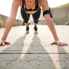 Kobieta w sportowym stroju wykonuje pompki na kolanach, słuchając muzyki przez słuchawki.
