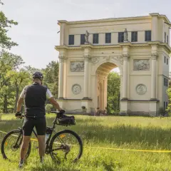 Rowerzysta przed łukiem triumfalnym. Piękne trasy rowerowe Czech zachęcają do odkrywania zabytków.