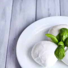 Trzy kulki mozzarelli z listkami bazylii na białym talerzu. Idealne do sałatki, a ich mozzarella kcal są niskie.