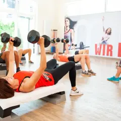 Ludzie ćwiczą z hantlami na ławkach. Czy cardio pomaga schudnąć? Tak, regularne ćwiczenia, jak te, wspierają redukcję wagi.