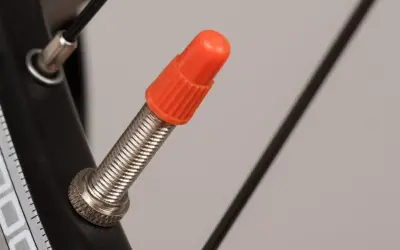 Pomarańczowa nakrętka na wentylu DV rowerowym, chroniąca przed zabrudzeniem.
