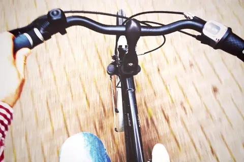 Widok z perspektywy rowerzysty. Ręka na kierownicy, dżinsy i droga w tle. Jak ustawić kierownicę w rowerze?