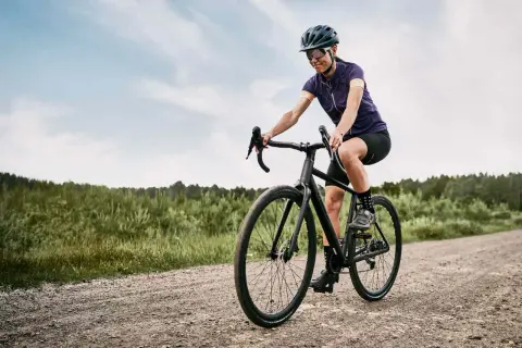 Kobieta na rowerze pokonuje szutrową drogę, ciesząc się jazdą w stylu gravel czy cross.
