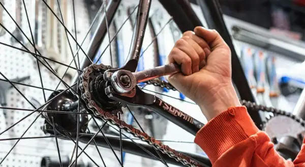Rowerzysta dokręca kluczem śrubę przy kole. Zastanawiasz się, ile kosztuje centrowanie koła w rowerze?