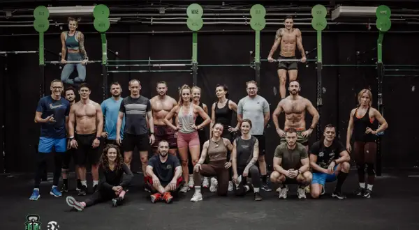 Grupa osób w strojach sportowych pozuje na tle sali treningowej CrossFit.