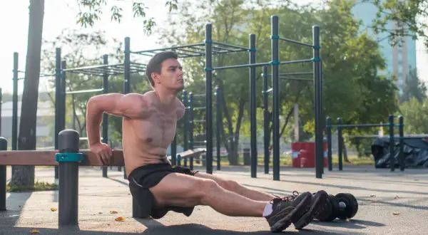 Mężczyzna wykonuje pompki na triceps na ławce na siłowni plenerowej.