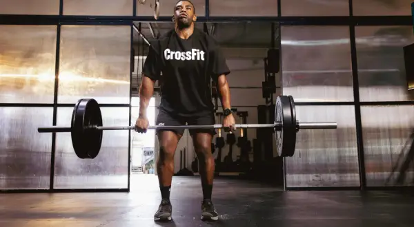 Mężczyzna w koszulce CrossFit podnosi sztangę na siłowni.