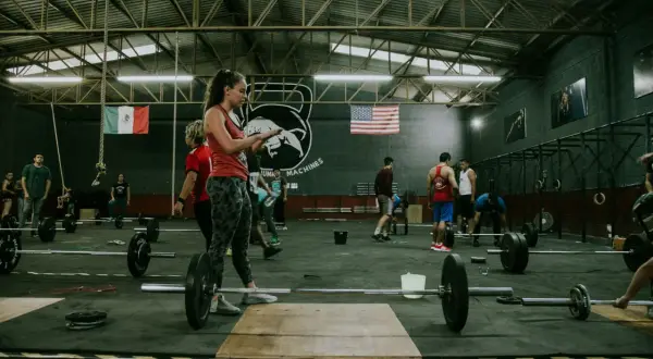 Ludzie ćwiczą w siłowni crossfit. Zastanawiasz się, crossfit po jakim czasie efekty? Widoczni są zawodnicy i sprzęt do treningu.