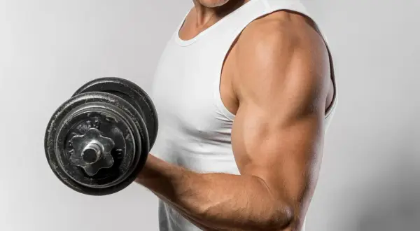 Mężczyzna w białej koszulce podnosi ciężarek, ćwicząc biceps. Zastanawiasz się, ile razy w tygodniu ćwiczyć biceps?