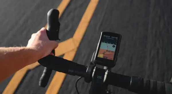 Dłoń trzymająca kierownicę roweru z zamontowanym licznikiem GPS pokazującym mapę.