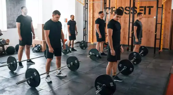 Mężczyźni w czarnych strojach ćwiczą z ciężarami w sali treningowej. Czy crossfit jest zdrowy? Ta grupa wydaje się to sprawdzać.
