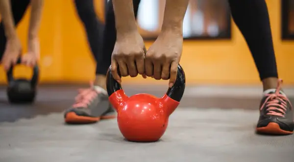 Dłonie zaciskają się na czerwonym kettlebellu. To część treningu fitness, co to za ćwiczenie?