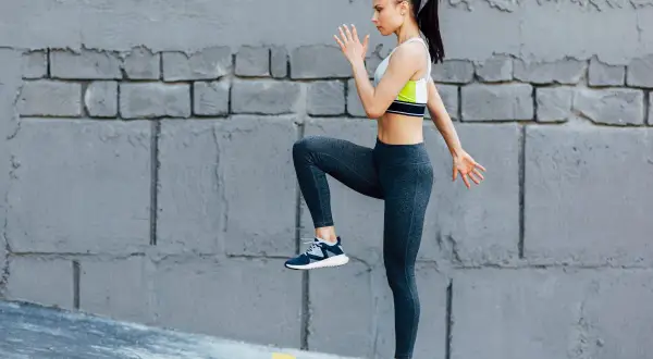 Kobieta w sportowym stroju wykonuje ćwiczenia cardio, podnosząc kolano.