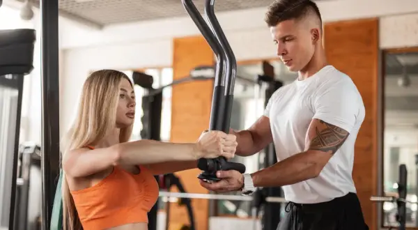 Trener personalny pomaga kobiecie ćwiczyć na siłowni. To inspiracja, jak zostać trenerem crossfit i motywować innych do aktywności.