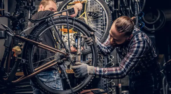 Dwóch mechaników pracuje nad rowerem w warsztacie. Jeden z nich dokonuje konserwacji roweru, dokręcając śruby kluczem.