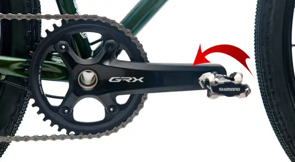 Czerwona strzałka pokazuje kierunek obrotu, by dowiedzieć się, jak odkręcić pedały w rowerze. Widoczny mechanizm korbowy Shimano GRX.
