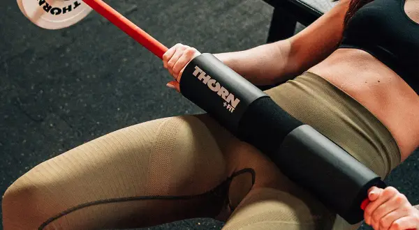 Kobieta wykonuje ćwiczenie hip thrust z gryfem i podkładką.