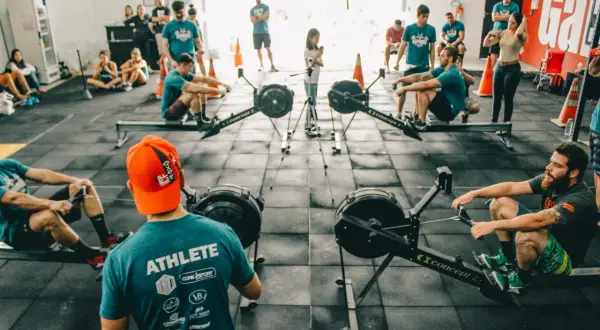 Ludzie trenują na wioślarzach w sali treningowej. Szukasz crossfit Warszawa gdzie? To miejsce jest idealne!