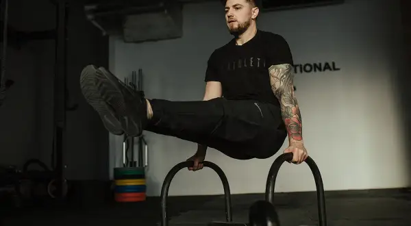 Mężczyzna wykonuje ćwiczenie na poręczach, pokazując, jak połączyć crossfit z siłownią.
