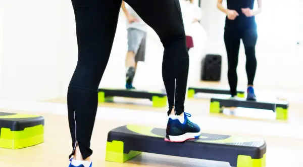 Kobieta w czarnych legginsach ćwiczy na stepperze w sali fitness.