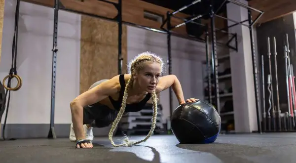 Kobieta wykonuje pompki z piłką lekarską, ćwicząc siłę i wytrzymałość. To świetny sposób, jak trenować crossfit.