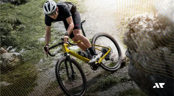 Kolarz na żółtym rowerze gravel pokonuje kamienisty szlak. To właśnie gravel, czyli rower do jazdy po różnym terenie.