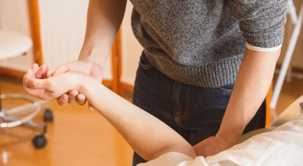 Fizjoterapeuta pomaga pacjentowi w ćwiczeniach po zabiegu cieśni nadgarstka, delikatnie masując przedramię.