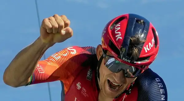 Michał Kwiatkowski, kolarz, triumfuje z zaciśniętą pięścią na tle błękitnego nieba.