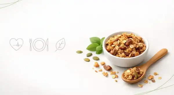 Chrupiąca granola w miseczce i na łyżce, obok pestki dyni i listki bazylii. To idealny pomysł na zdrowe śniadanie.