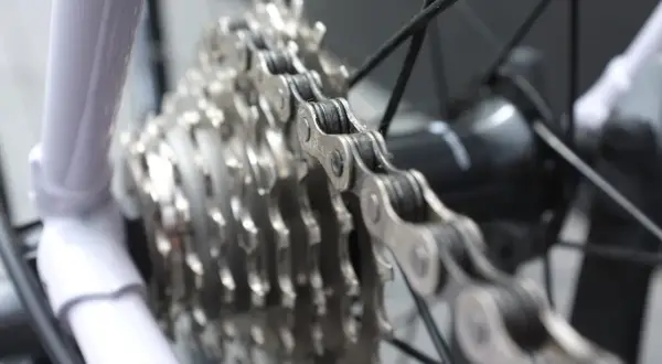 Biała rama roweru, metalowy łańcuch i zębatki tworzą mechanizm wolnobiegu.